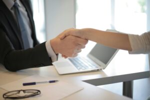 A hand is reaching out over a computer shaking someone else's hand
