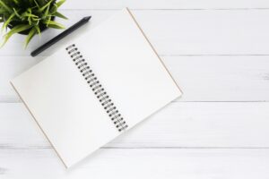 An open notebook next to a plant, on a table